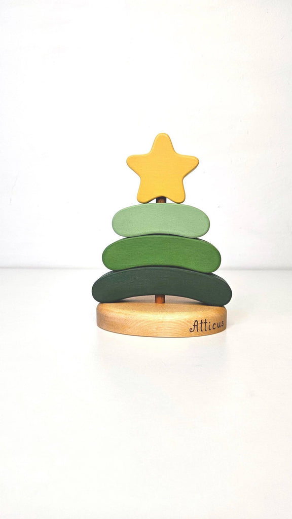 The Handmade Wooden Stacking Toy Green Christmas Tree features three green layers, a yellow star topper, and "Atticus" engraved on the wooden base—an eco-friendly holiday toy.