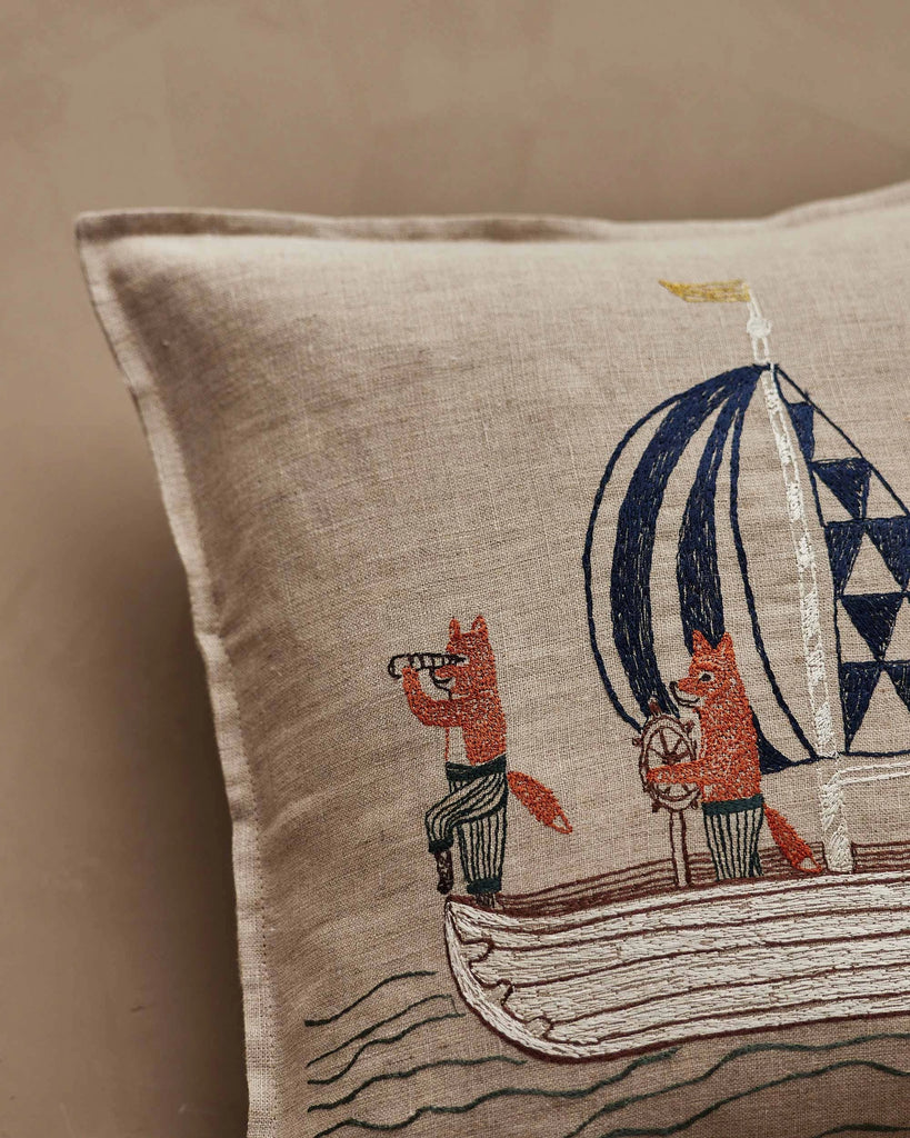 The Coral & Tusk Sailing Foxes Pillow features two embroidered foxes on a sailboat—one with a spyglass, the other steering—plus a blue and white geometric sail and wavy water lines for a charming nautical touch.