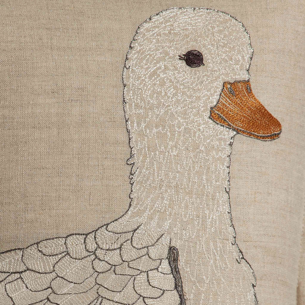 Close-up of a textured embroidery of a Coral & Tusk Mama Duck on a decorative pillow, featuring intricate white stitching for the body and a detailed orange beak on a beige fabric background.