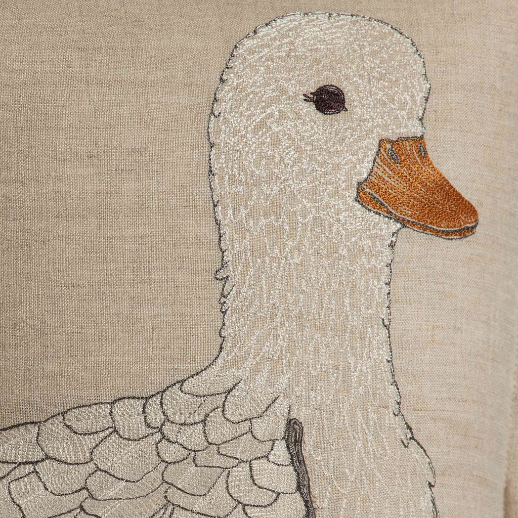 The Coral & Tusk Mama Duck Pocket Pillow features detailed embroidery of a white duck with an orange beak on beige fabric, highlighting feathers and facial features for a textured look—plus removable felt ducklings in the pocket.