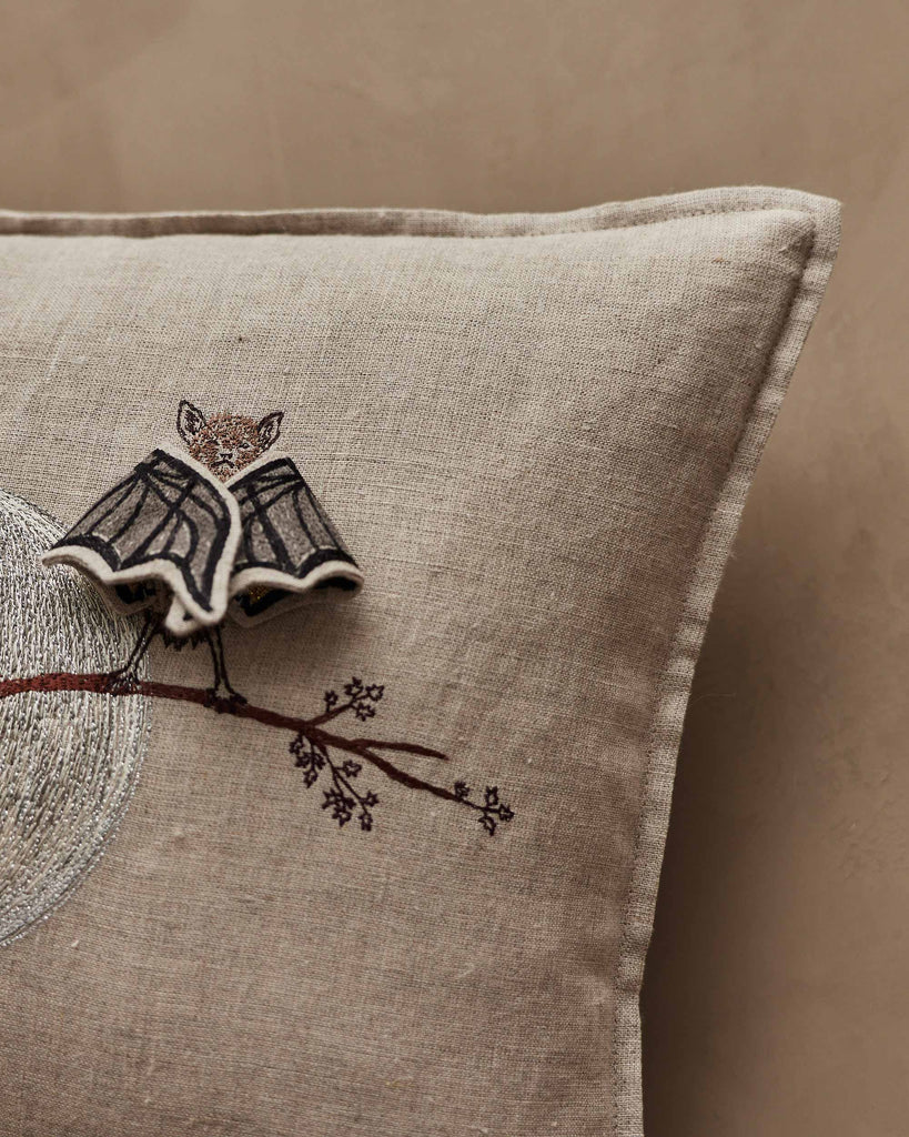 The Coral & Tusk Bat Branch Pillow features beige bat wings, an embroidered tree branch with baby bats, and a 3D bat brooch. Set against a neutral wall, it's perfect for Halloween décor. Ships in one week.
