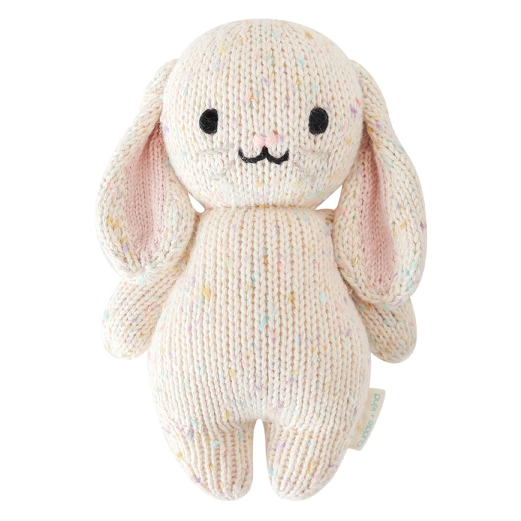 The Cuddle + Kind Baby Bunny is hand-knit from heirloom-quality Peruvian cotton yarn, featuring long floppy ears with pink insides, a cream body speckled with pastels, black eyes, and an embroidered nose and mouth.
