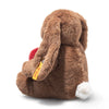 The Steiff Hoppie Rabbit – Love plush sits facing away, holding a red heart. It has a white tail, long ears with a yellow tag, and is set against a plain white background—a perfect gift for Steiff fans.