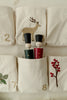 Two wooden peg dolls in black hats and painted uniforms sit in a cloth pocket marked with an 8 on the Sabo Concept Christmas Cotton Advent Calendar, which features embroidered branches and a deer on cream cotton.