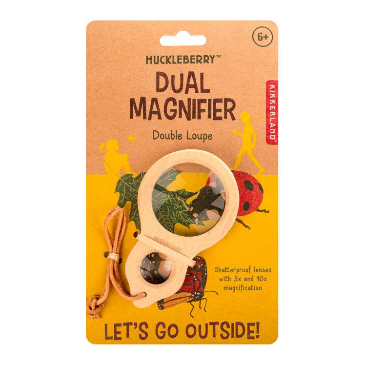 The Huckleberry Dual Magnifier has shatterproof lenses, a wooden handle, leather strap, and 5x/10x magnification. Its packaging shows leaves, a ladybug, children exploring, and the phrase "LET'S GO OUTSIDE!.