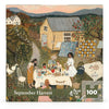 In the September Harvest Mini - 100 Piece Mini Puzzle, a group of people gathers for an outdoor meal near a cottage, with a quilt hanging on a clothesline and geese nearby.