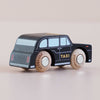 A small wooden toy taxi, the No. 45 GT275 Bertie made in England, styled as a classic London black cab with “TAXI” written on the side, sits on a light-colored surface. The plain wooden wheels feature “LETOYVAN” printed on them.