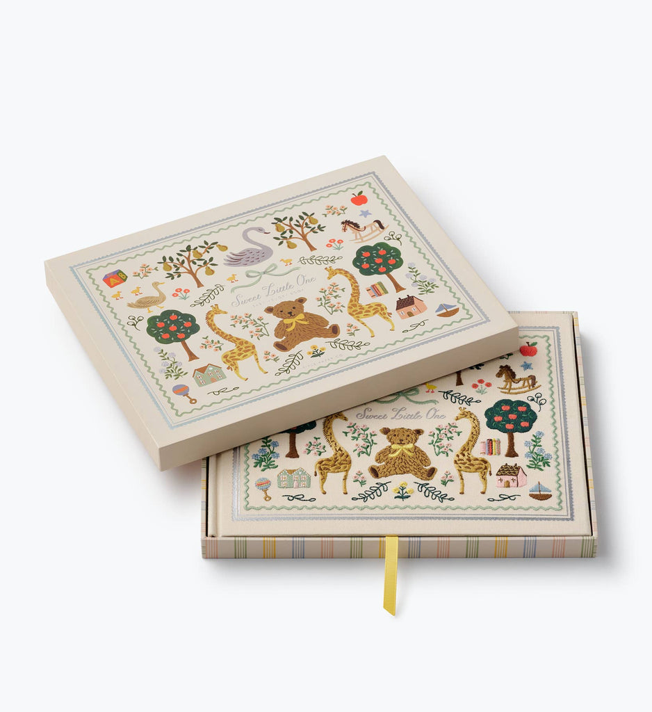 Two decorative boxes featuring enchanting illustrations of animals, trees, and books on the lids. These cream-colored boxes showcase vibrant, whimsical designs and include a yellow ribbon inside one box—perfect for storing treasured items such as your Storybook Embroidered Baby Book or other cherished keepsakes.