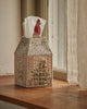 The Coral & Tusk Home for the Holidays Tissue Box Cover, shaped like a house with festive embroidery, features a Christmas tree, windows, and a person in winter clothing holding a tissue on the windowsill.