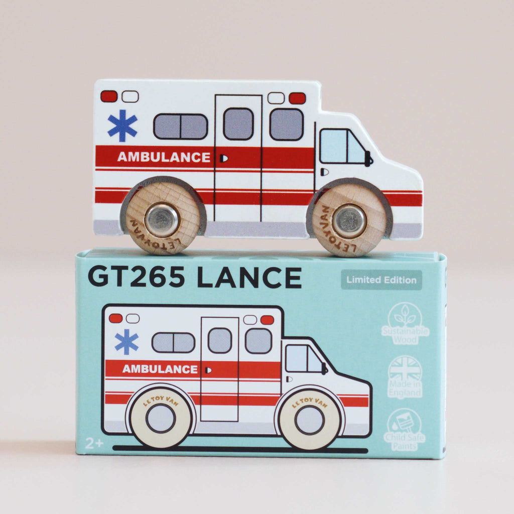 A wooden toy ambulance with red stripes sits atop its packaging, which features an illustrated version of the toy and the name “No. 43 GT265 Lance | Made in England.” Perfect for imaginative play and rescue adventures, the box highlights that it’s made from sustainable wood and designed for ages 2 and up.