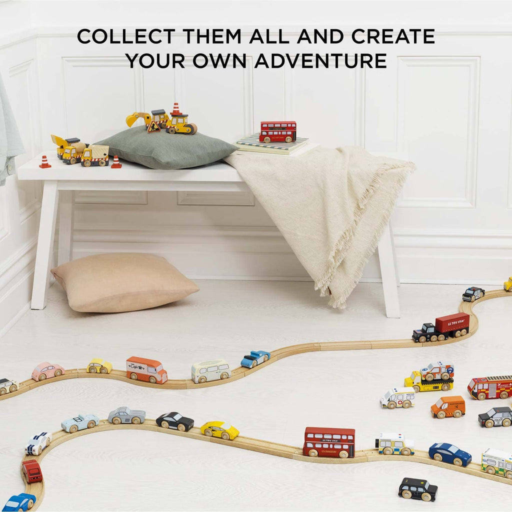 The Emergency Helicopter & Rescue Cars wooden toy set, featuring colorful rescue vehicles, is arranged in a wavy pattern on the floor. A bench with a pillow, cushion, and blanket sits behind. Text: "COLLECT THEM ALL AND CREATE YOUR OWN ADVENTURE.