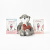 A Slumberkins Otter Kin + Lesson Book - Family Bonding toy holding a red heart, made from hypoallergenic fiberfill, flanked by two illustrated books titled "otter’s community grows" and "otter", set against