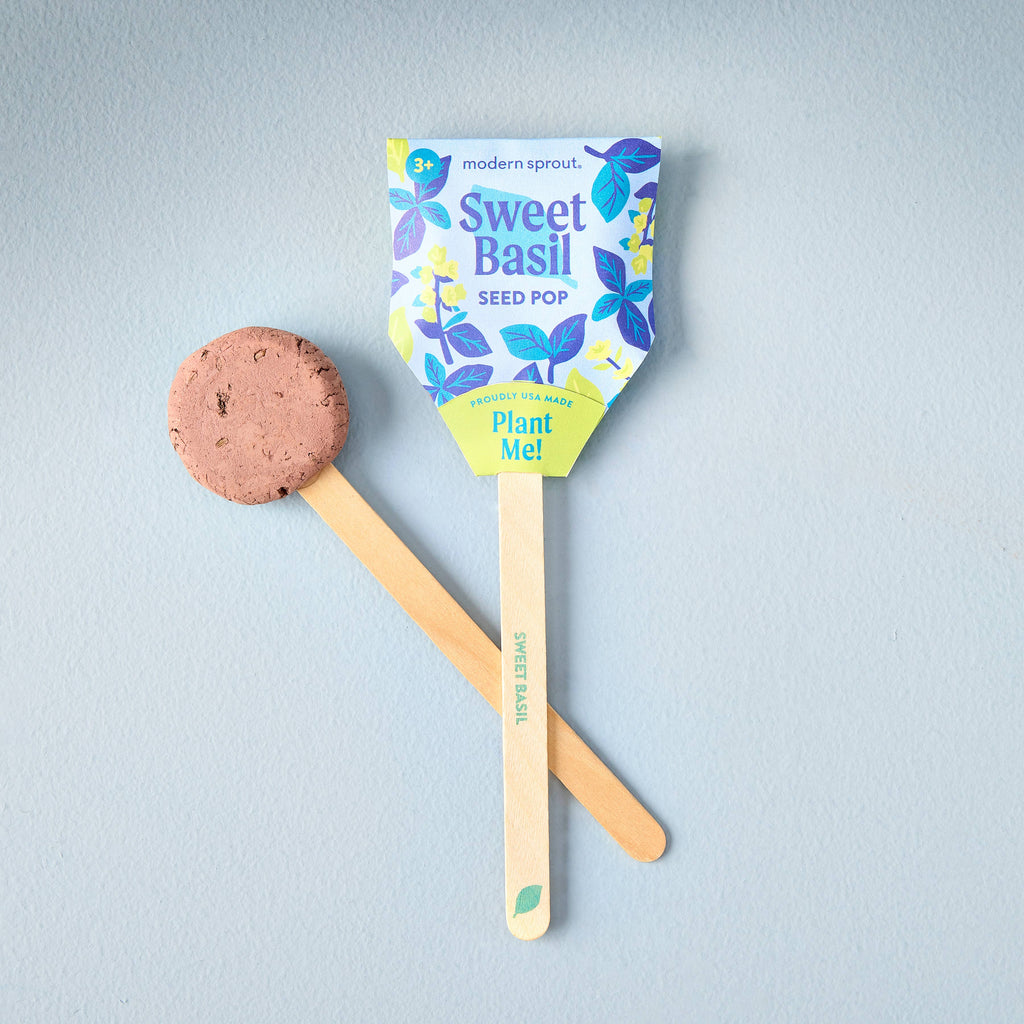 The Garden Seed Pop (Single) is perfect for starting a vegetable garden or family gardening, featuring a wooden stick, soil pellet, and packaging with blue leaves and yellow flowers that says “Sweet Basil Seed Pop – Plant Me!”.
