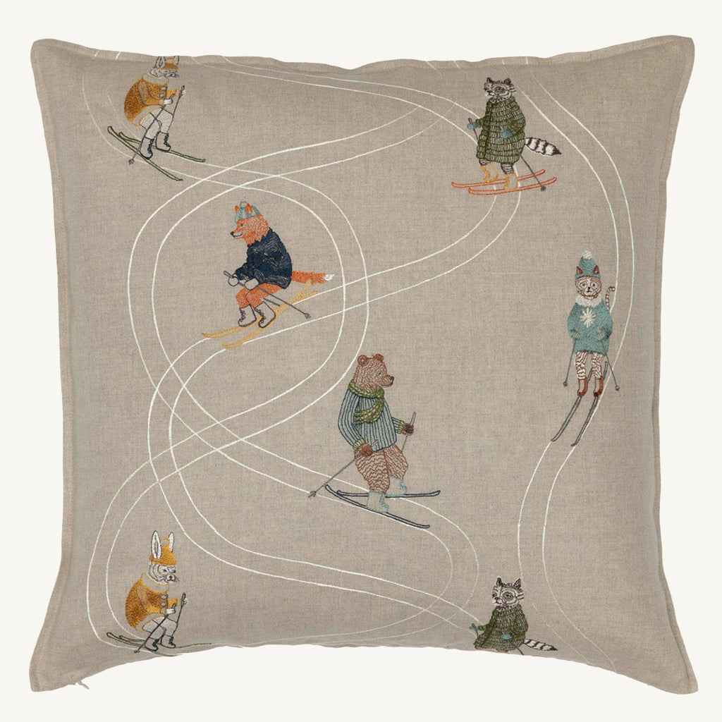 The Coral & Tusk Downhill Skiers Pillow is a square beige embroidered cushion featuring a fox, raccoon, rabbit, and bear skiing in different directions with white stitched ski trails.