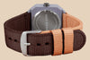 A close-up of the back of a Mini Kyomo Watch - Plum Cake with a two-tone brown and tan fabric strap, stainless steel engraved back, and a silver buckle.
