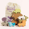 A set of colorful wooden animal blocks featuring woodland creatures—including a bear, squirrel, turtle, rabbit, deer, and more—is stacked in front of a cloth bag labeled "Woodland Stacking Forest Animals & Bag." This sustainable toy offers stacking fun with a variety of forest animals.