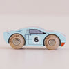 No. 26 GT145 Fred | Made in England is a light blue classic toy car in the style of a wooden racing car, featuring the number 6 on the side, wooden wheels marked “LetoYVan,” and simple black and white detailing, all set against a pale background.
