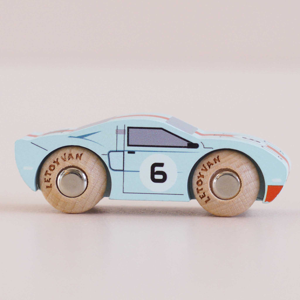 No. 26 GT145 Fred | Made in England is a light blue classic toy car in the style of a wooden racing car, featuring the number 6 on the side, wooden wheels marked “LetoYVan,” and simple black and white detailing, all set against a pale background.