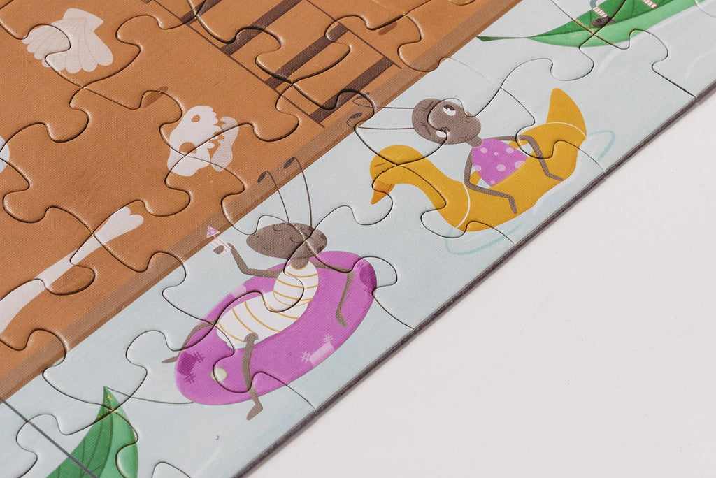A close-up of the Beneath the Branches 200 Piece Puzzle shows cartoon ants relaxing on pool floats—one on a purple ring with a drink, another on a yellow duck—all crafted from matte pieces with green leaves and water in the background.
