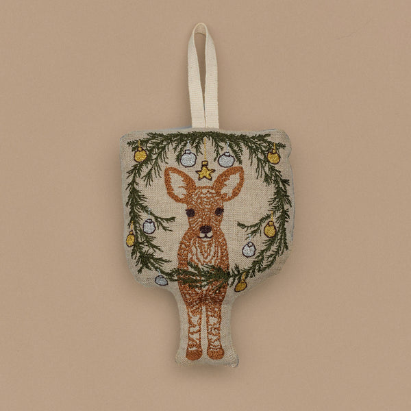 The Togetherness Deer Ornament features a fawn surrounded by a garland of green branches and ornaments, elegantly hanging on a loop against a beige backdrop.