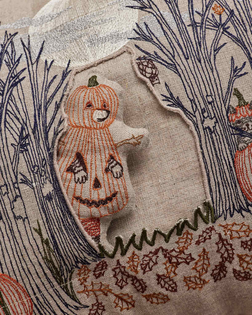 Embroidery of a bear in a pumpkin costume peeks from a felt cutout, surrounded by stitched trees and autumn leaves on the Coral & Tusk Spooky Forest Pocket Pillow.