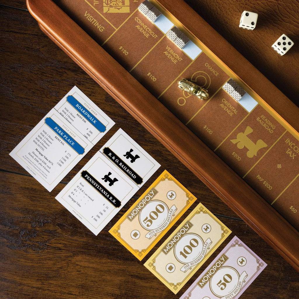 The Monopoly Luxury Edition is displayed on a wooden table with cards, two dice, die-cast tokens, railroad property cards, and colorful Monopoly money.