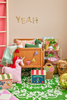 A colorful children’s room features a crib, plush unicorn pillow, patterned boxes, a dragon toy, books, a wicker bear basket, and a green patterned rug. Next to the crib is the charming Raffia Kids Bag with Circus Theme, sustainably handmade from raffia. The word “YEAH” decorates the wall above the crib.