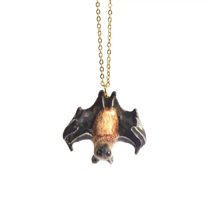 A Fruit Bat Necklace with a bronze-tinted body hanging from a golden chain, featuring a hand-painted charm, set against a plain white background.