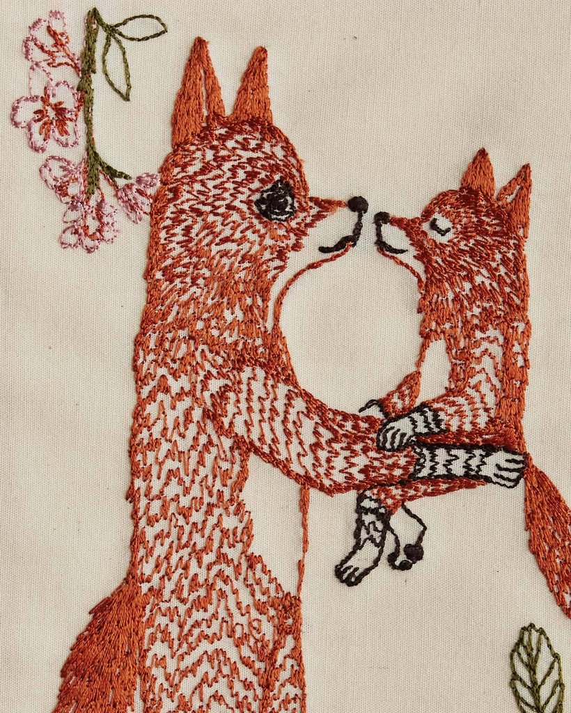 The Coral & Tusk Fox Mama Card features two foxes facing each other, with the larger fox holding the smaller. Pink flowers and green leaves are embroidered on cream-colored fabric, making a charming keepsake or new parent gift.