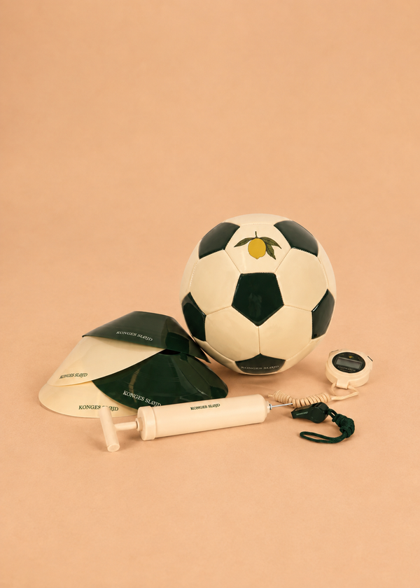 The Konges Sloejd Football Set—featuring a soccer ball, two black-and-white training cones, a stopwatch with a cord, and a hand pump—is arranged on a light brown surface, providing everything you need for the perfect backyard practice football activity.