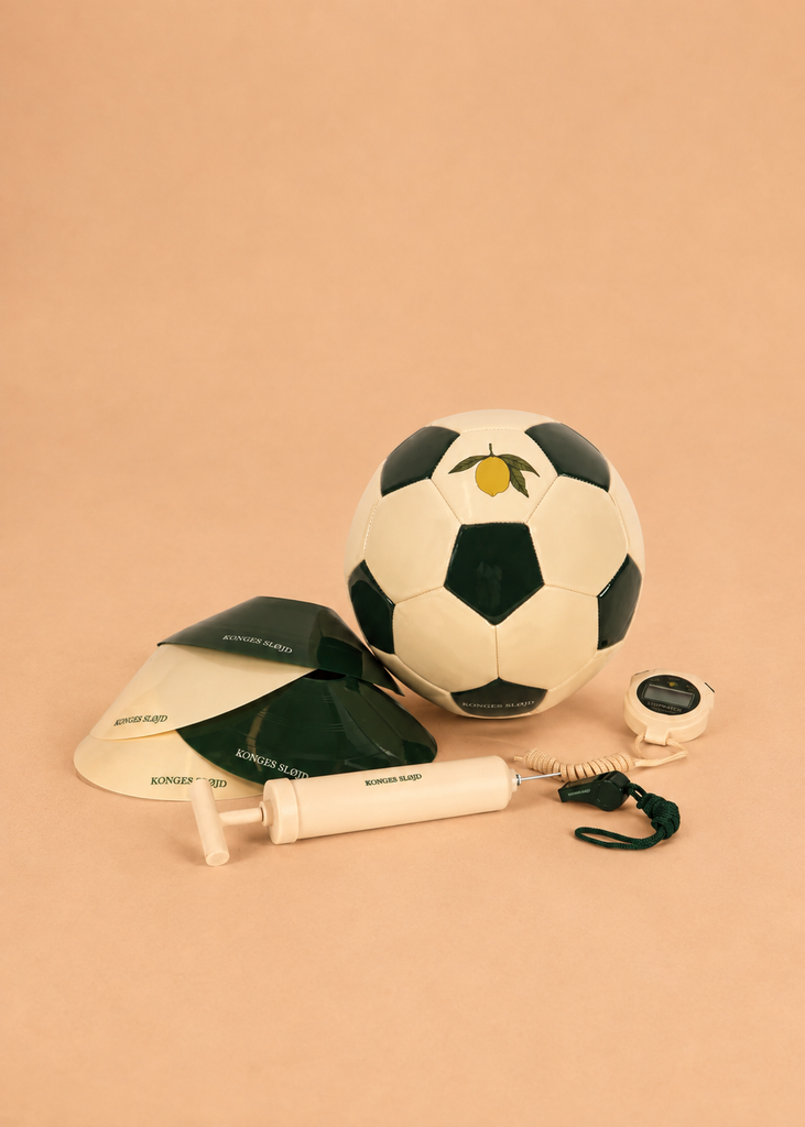 The Konges Sloejd Football Set—featuring a soccer ball, two black-and-white training cones, a stopwatch with a cord, and a hand pump—is arranged on a light brown surface, providing everything you need for the perfect backyard practice football activity.