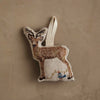 The Coral & Tusk Deer with Lights Ornament is a woodland-inspired deer ornament with embroidered details and a blue bird perched on string lights, hanging by a loop against a beige background—perfect for your Christmas tree.