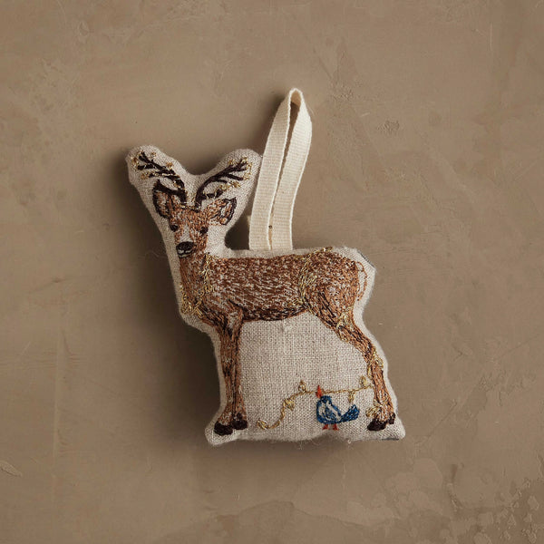 The Coral & Tusk Deer with Lights Ornament is a woodland-inspired deer ornament with embroidered details and a blue bird perched on string lights, hanging by a loop against a beige background—perfect for your Christmas tree.