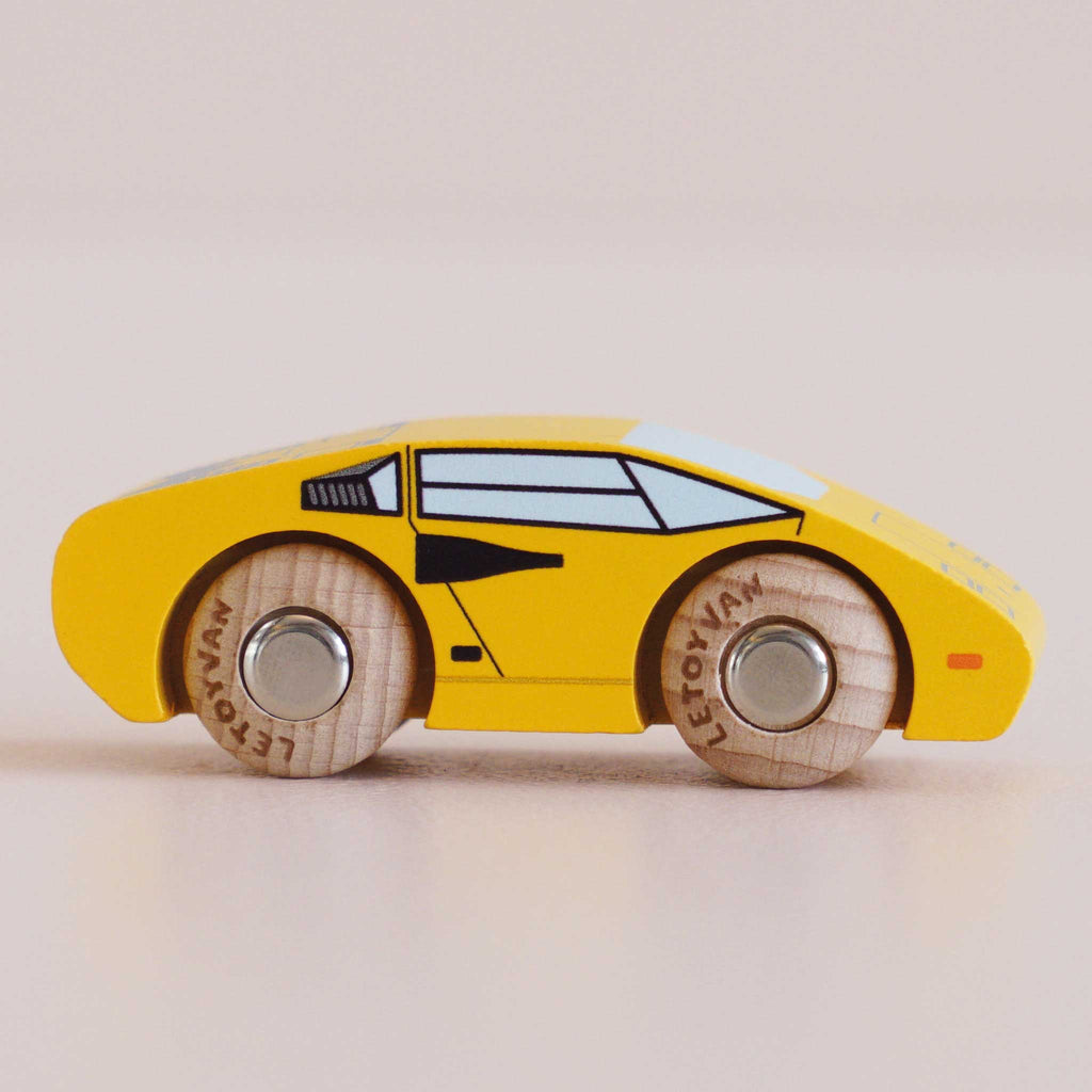 The No. 14 GT80 Lando, a yellow wooden toy car made in England, is shown in a side view on a light surface. Crafted with painted windows and details and featuring two wooden wheels, this charming racing toy offers hours of safe play with its child-safe finish.
