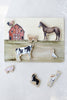 A delightful *Farm Animals Wooden Puzzle: A Tabitha Paige Puzzle* featuring a vibrant red barn and removable animal pieces—a horse, cow, sheep, pig, dog, rooster, goose, and alpaca—displayed on a light surface. This educational puzzle is the perfect toddler toy for developing fine motor skills and introducing children to farm animals.