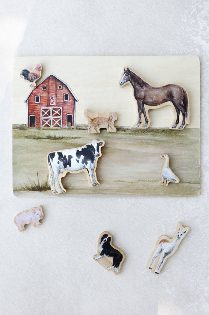 A delightful *Farm Animals Wooden Puzzle: A Tabitha Paige Puzzle* featuring a vibrant red barn and removable animal pieces—a horse, cow, sheep, pig, dog, rooster, goose, and alpaca—displayed on a light surface. This educational puzzle is the perfect toddler toy for developing fine motor skills and introducing children to farm animals.