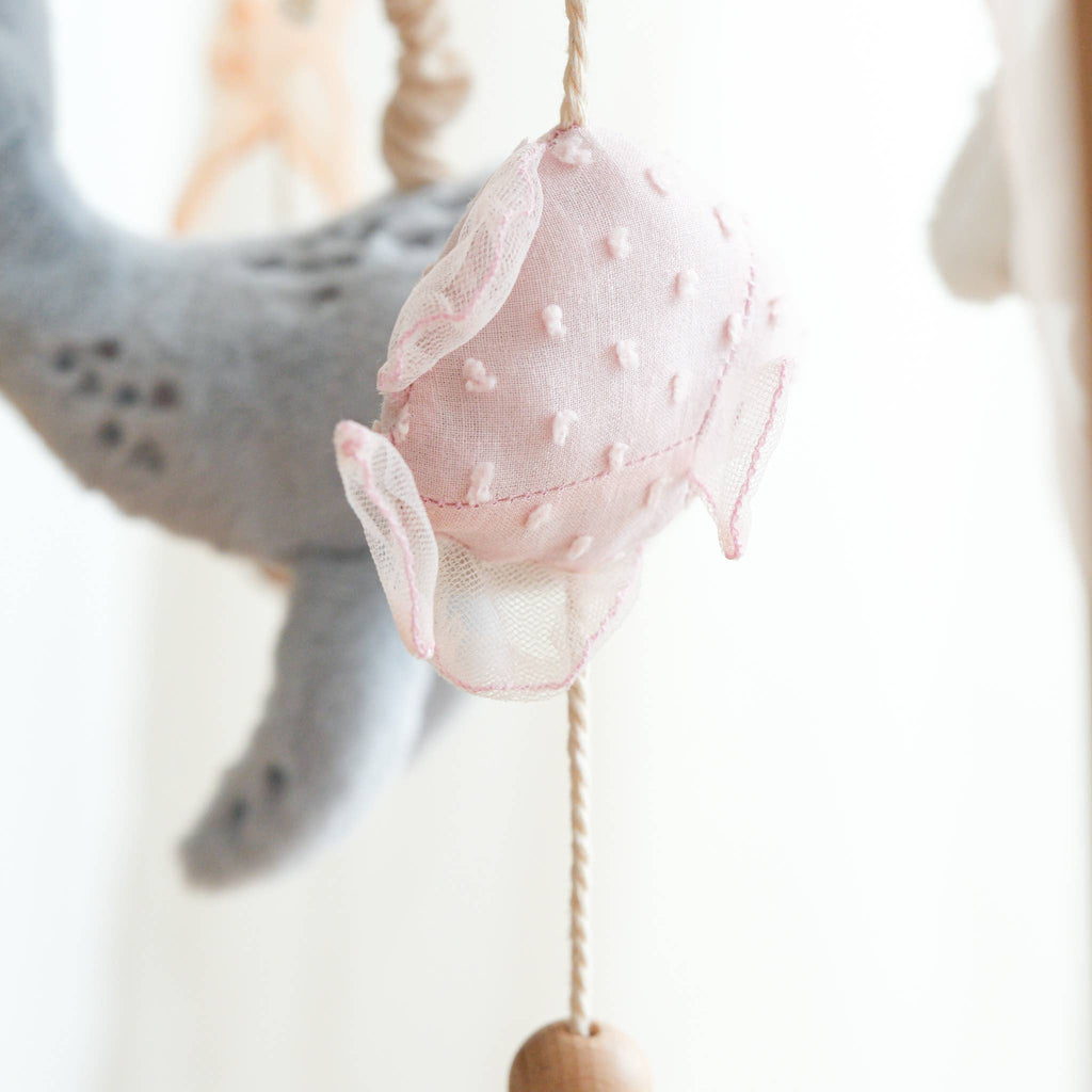 The Nautical Dreams Mobile features a soft, pink, polka-dotted fish plush with mesh fins hanging from a string, adding charming nautical style to your nursery decor.