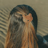 A close-up of a person's head from behind, showing their brown hair secured with Donsje Leather Hair Ties - Bear on a sandy beach background.