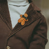 A close-up of a person wearing a dark brown corduroy jacket with a white turtleneck underneath, adorned with a small, cute Donsje Wonda Gingerbread hairclip on the lapel.