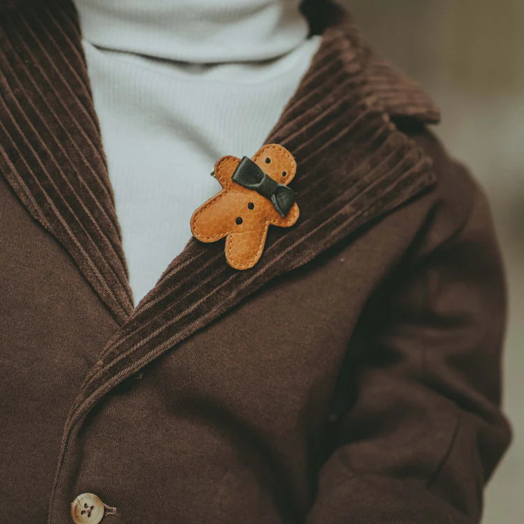 A close-up of a person wearing a dark brown corduroy jacket with a white turtleneck underneath, adorned with a small, cute Donsje Wonda Gingerbread hairclip on the lapel.