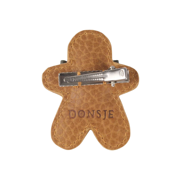 A handmade leather Donsje Wonda hairclip in the shape of a gingerbread man, with a metal clip, engraved with the brand name "Donsje.