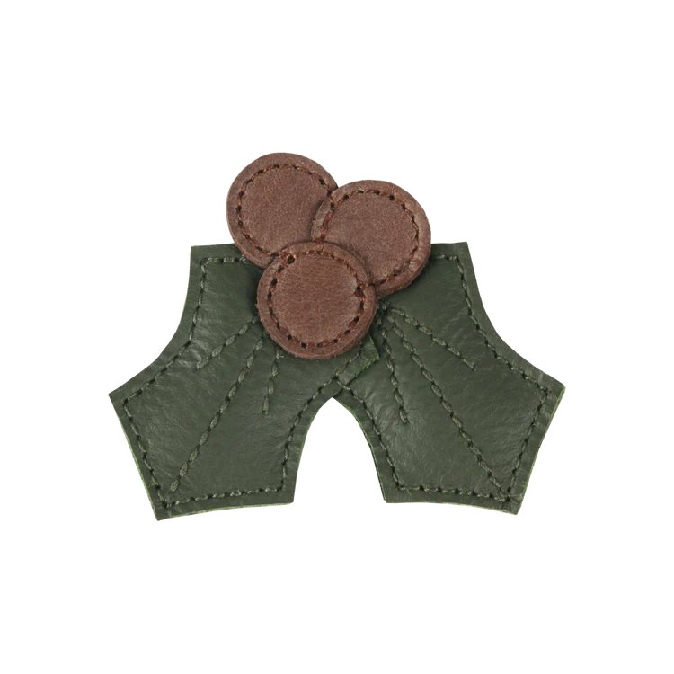 A pair of green leather medieval-style bracers with three Donsje Wonda Hairclips | Holly arranged in a triangle pattern, isolated on a white background.