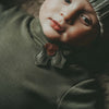 Close-up of a baby wearing a gray knitted hat, adorned with a Donsje Wonda Hairclip | Holly, and green shirt with a decorative brown and green ribbon, gazing upward with a thoughtful expression.