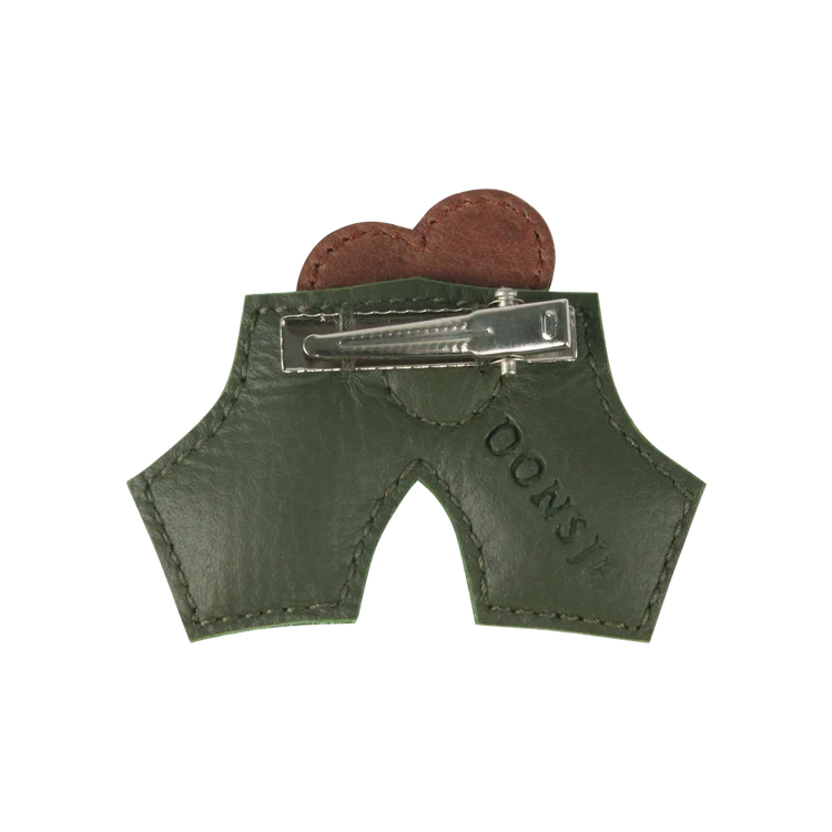 Two chocolate cookies peek out from a small, green leather Donsje Wonda Hairclip | Holly with a zipper, embossed with the word "cookies." The pouch, resembling a pair of pants, is designed as a festive hair accessory.