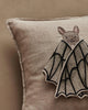 The Coral & Tusk Bat Wing Surprise Pillow is a beige linen cushion featuring an embroidered bat with its face and butterfly-like open wings on a neutral background.
