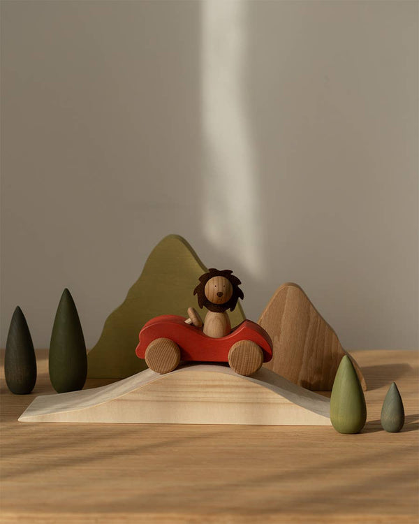 Sabo Concept First Journey features a small lion in a red car on a hill with green trees and brown mountains—perfect for open-ended play and inspiring imagination in natural light.