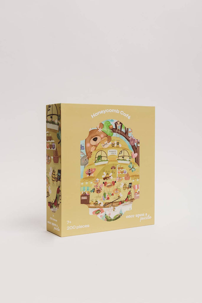 The Honeycomb Cafe 200 Piece Puzzle comes in a yellow upright box featuring whimsical animals in a café scene. Includes matte textured pieces; recommended for ages 7+. Box shown on a plain white background.