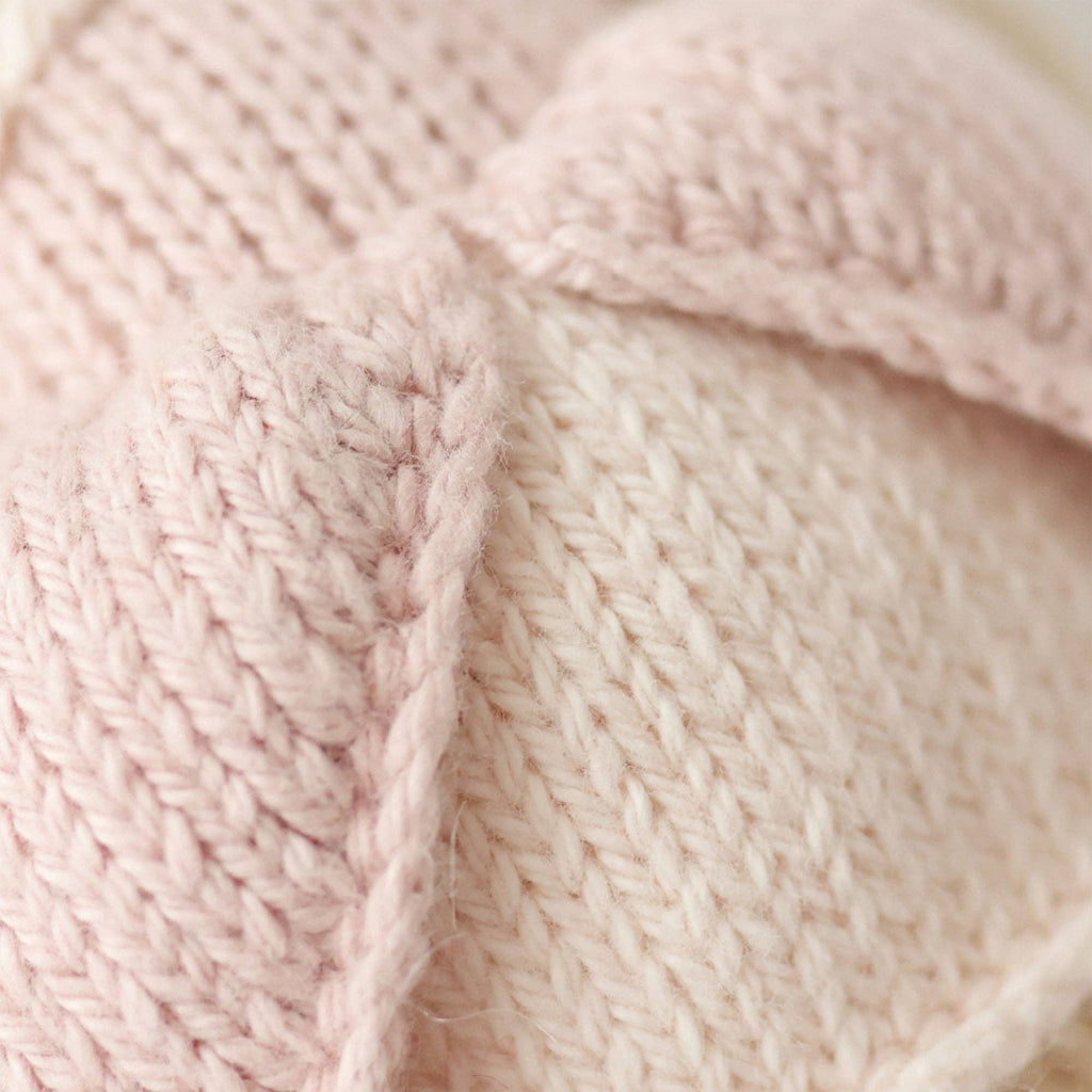 Close-up of the soft, light pink and cream yarn details in the hand-knit fabric of Cuddle + Kind Tiny Rose the Princess, a handmade doll crafted in Peru.