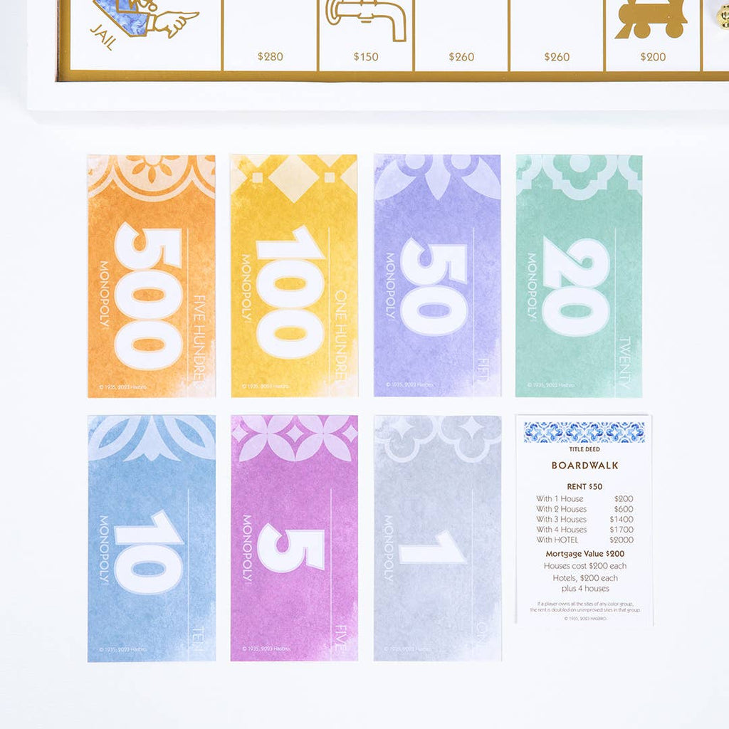 Seven colorful Monopoly Bianco Edition bills in denominations of 500, 100, 50, 20, 10, 5, and 1, arranged alongside a Boardwalk property deed card.