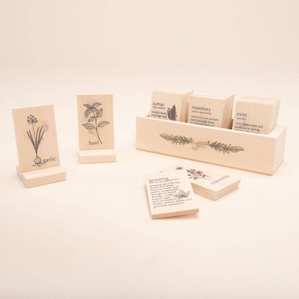 Introducing the Uncle Goose Chips - Herbs: a collection of wooden cards made from eco-friendly basswood, showcasing illustrated herbs such as garlic, basil, rosemary, mint, and sumac. These cards are elegantly presented in and around a wooden box decorated with an intricate leafy pattern on its side.